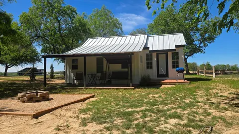 1914 HideAway exterior with a covered porch beneath shade trees