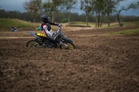Rider on a black motocross bike with yellow wheel spokes kicking up dirt through a Creekside turn