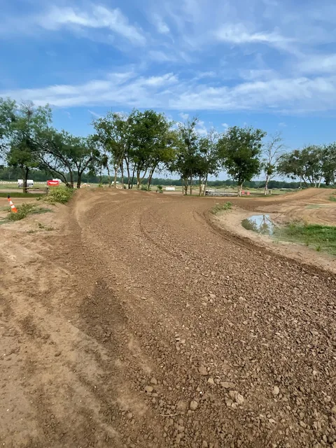 An open dirt corner at Creekside MX beneath a wide blue sky, with trees and trackside bleachers