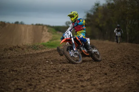 Rider in a yellow helmet guiding an orange number 17 bike around a berm, with another rider behind