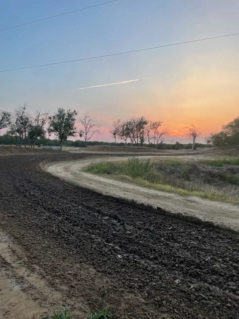 Freshly worked dirt sweeping around a Creekside MX berm beneath a pink and orange sunset