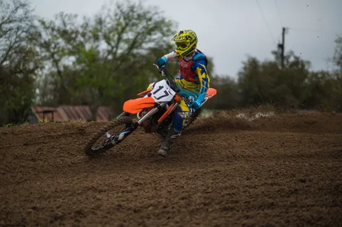 Rider wearing a bright yellow helmet and blue gear turning an orange number 17 bike through soft dirt
