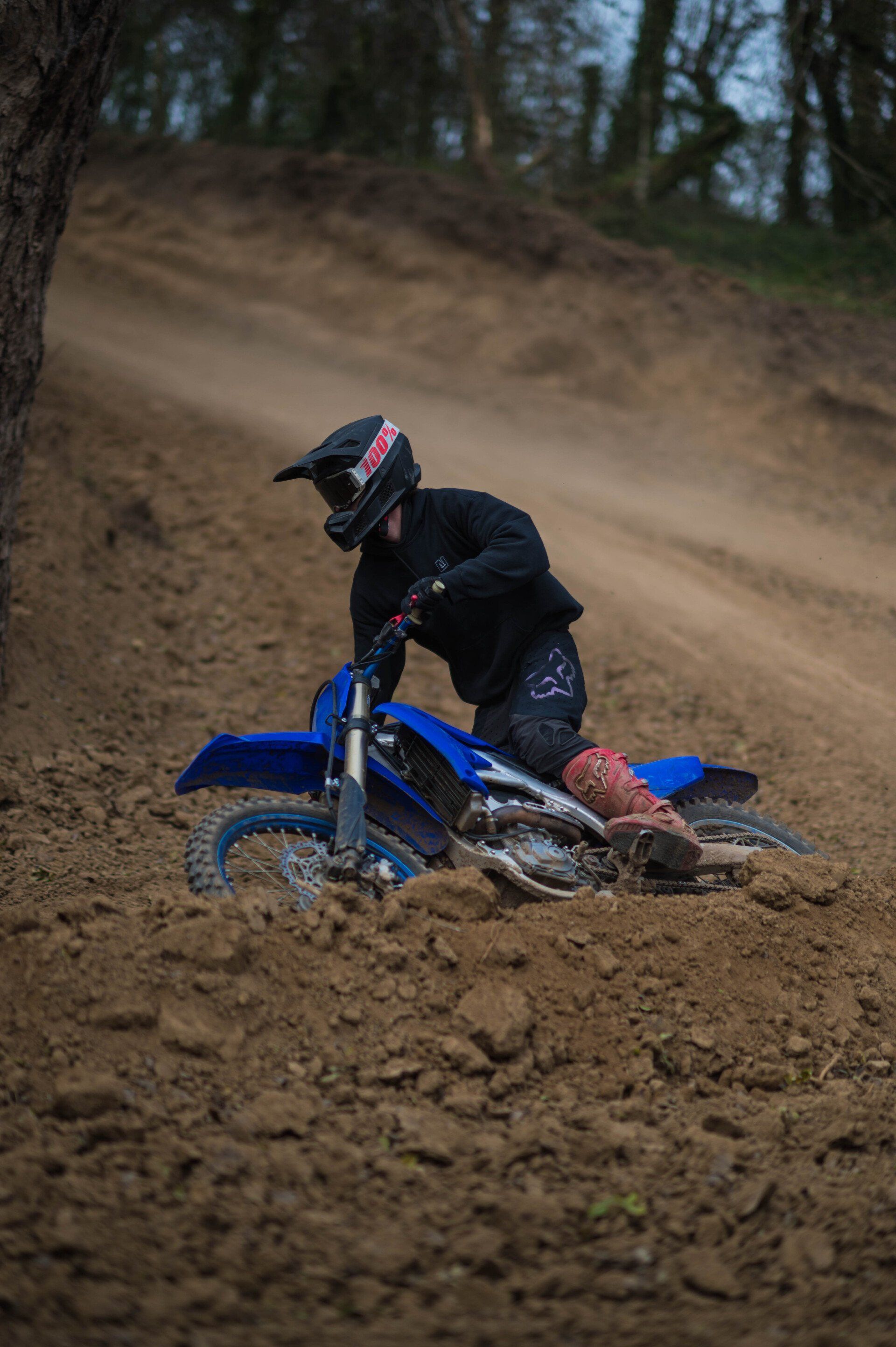 A rider on a blue dirt bike rounding a dirt turn at Creekside MX